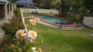 Un patio trasero con piscina, terraza cubierta y césped con flores.