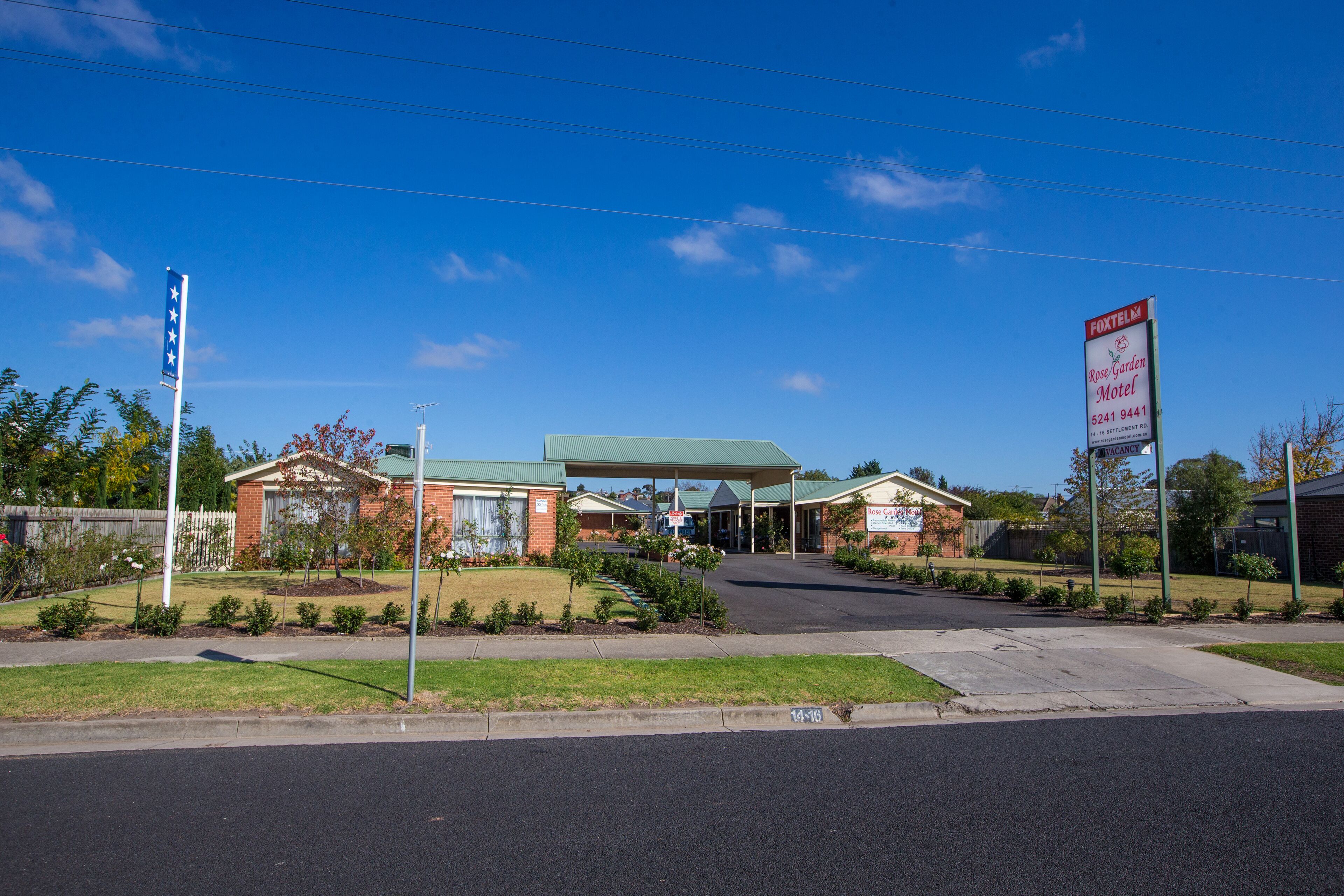 A Rose Garden Motel with a green roof, a parking lot, and a clear blue sky.