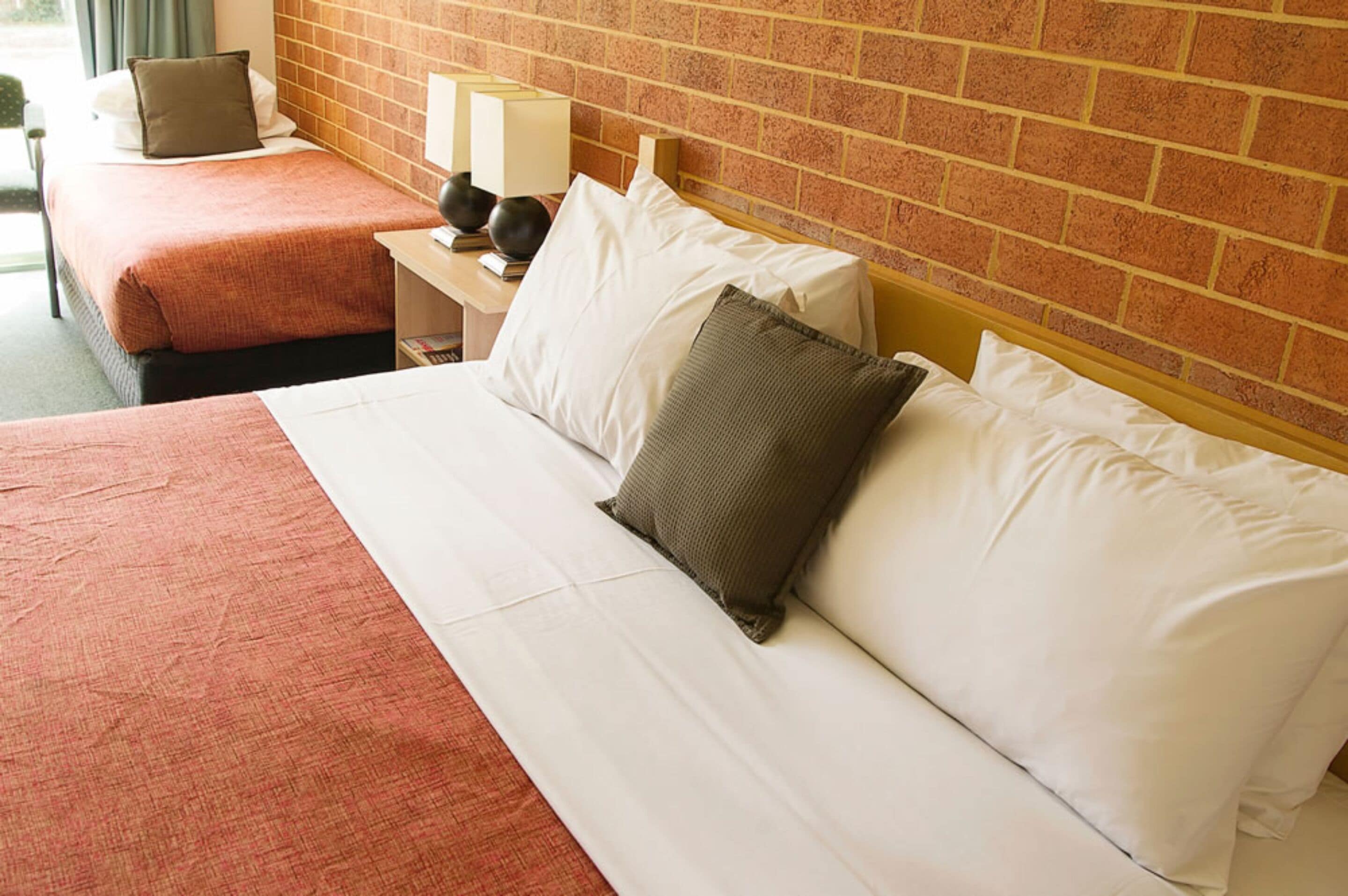 A hotel room with a large bed, a nightstand with a lamp, and a brick wall.