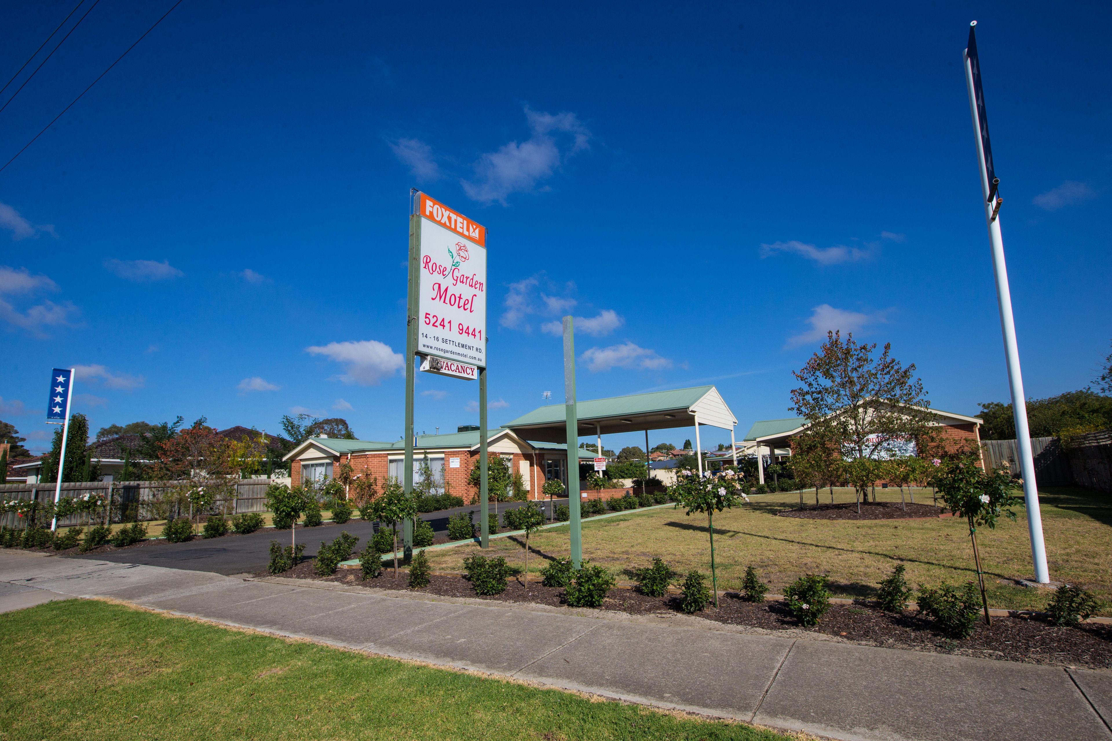 A motel with a large sign, a covered parking area, and a well-maintained lawn.