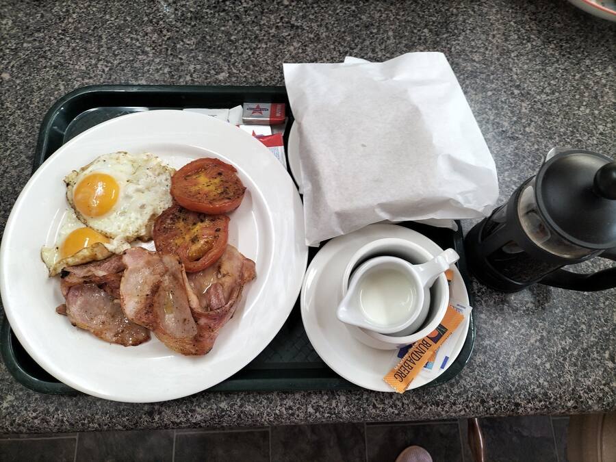 A breakfast tray with eggs, bacon, tomatoes, and a cup of coffee.
