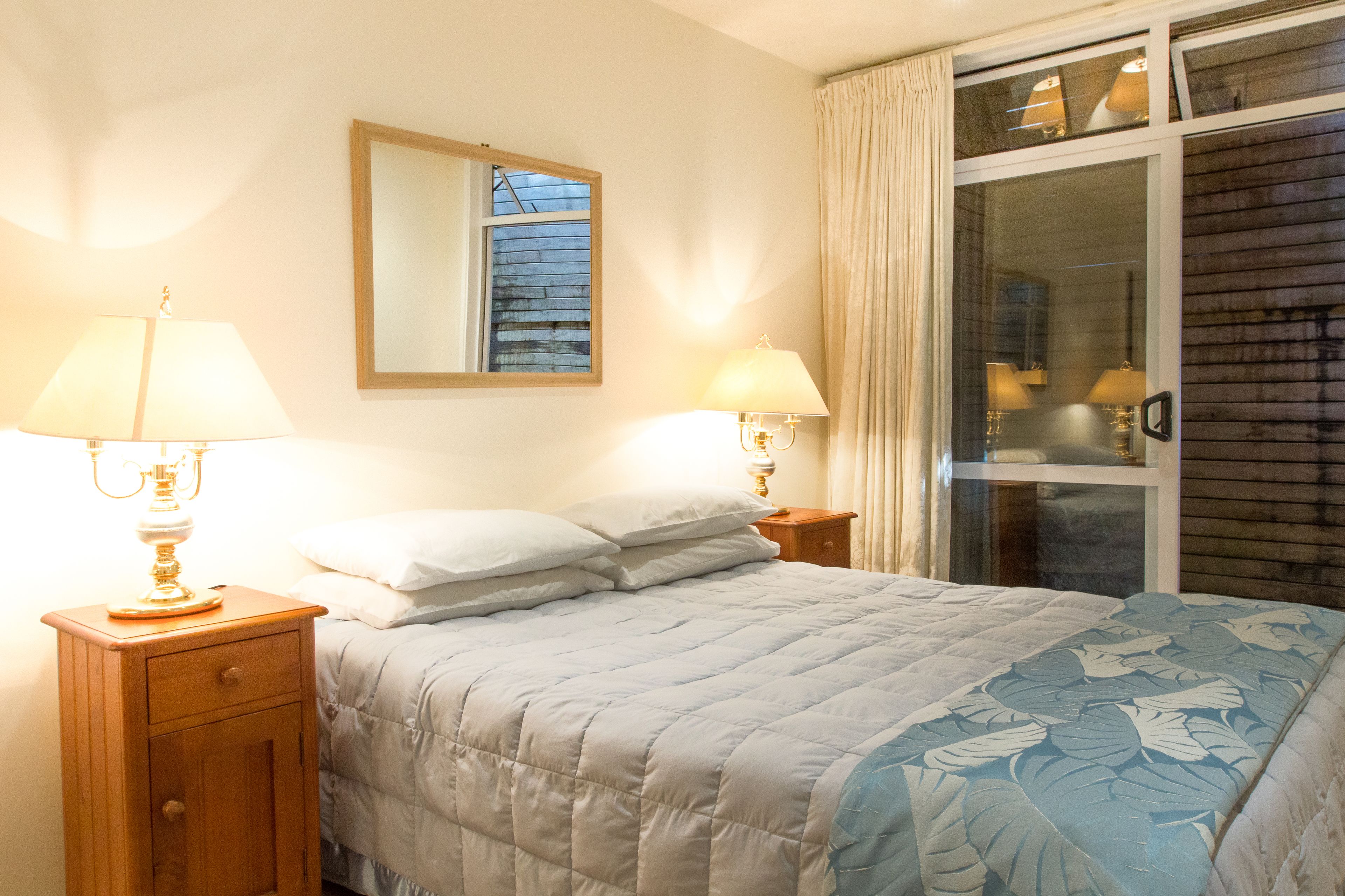 A bedroom with a bed, two bedside lamps, a nightstand, a mirror, and a window with curtains.