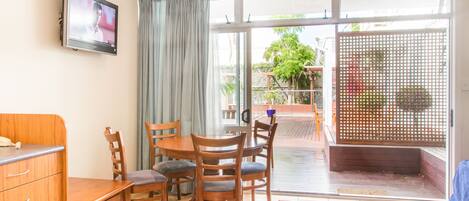 A room with a dining table, chairs, a TV mounted on the wall, a sliding glass door leading to an outdoor area, and a wooden cabinet.