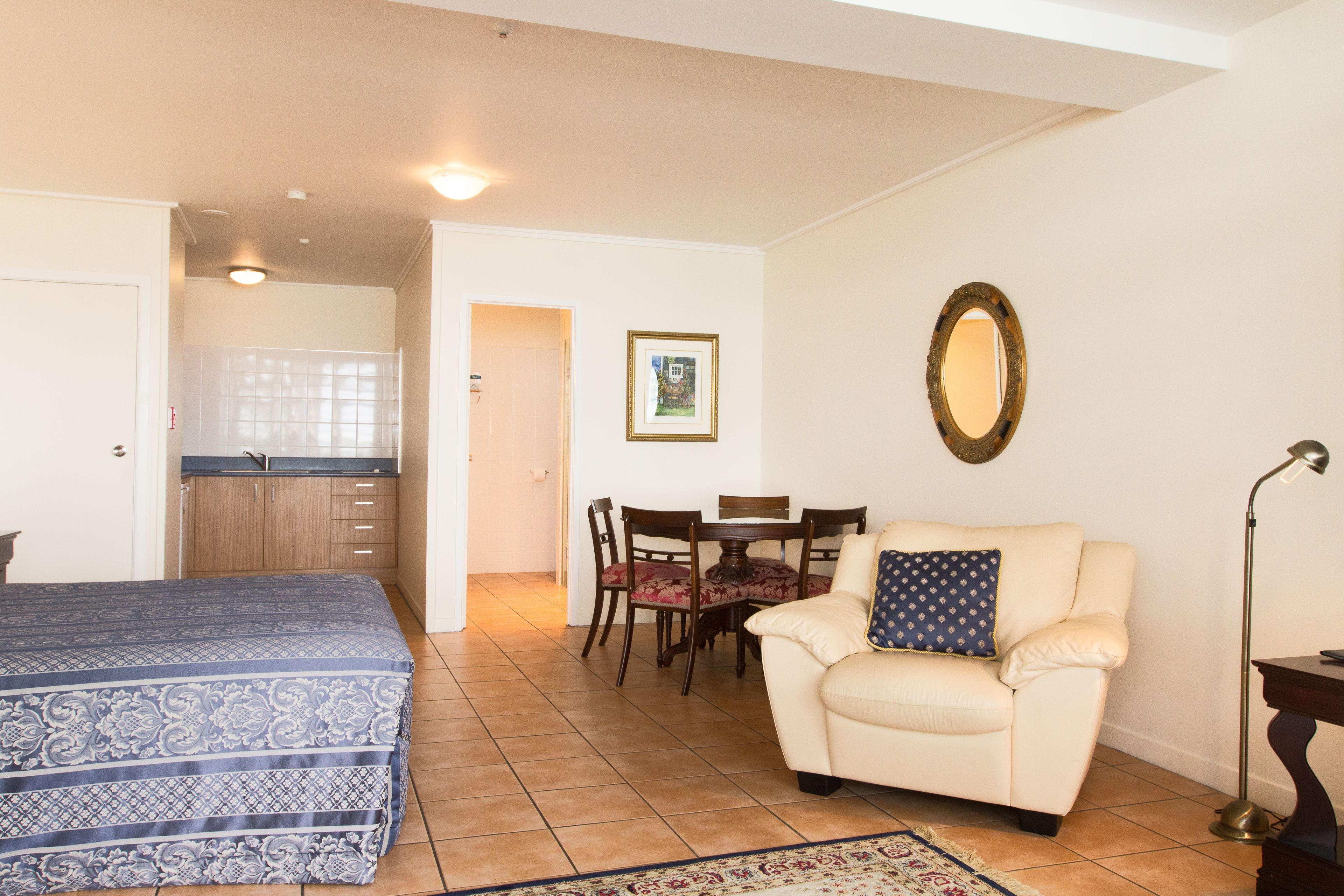 Un dormitorio con cama, una zona de estar con sillón y mesa, y una kitchenette.
