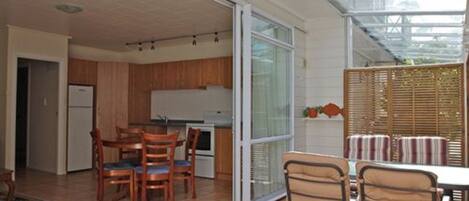 A modern kitchen with wooden cabinets, a dining area with a table and chairs, and a sliding glass door leading to an outdoor patio.