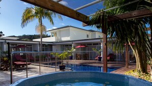 En swimmingpool med en træterrasse, liggestole og et receptionsområde med en rød parasol.
