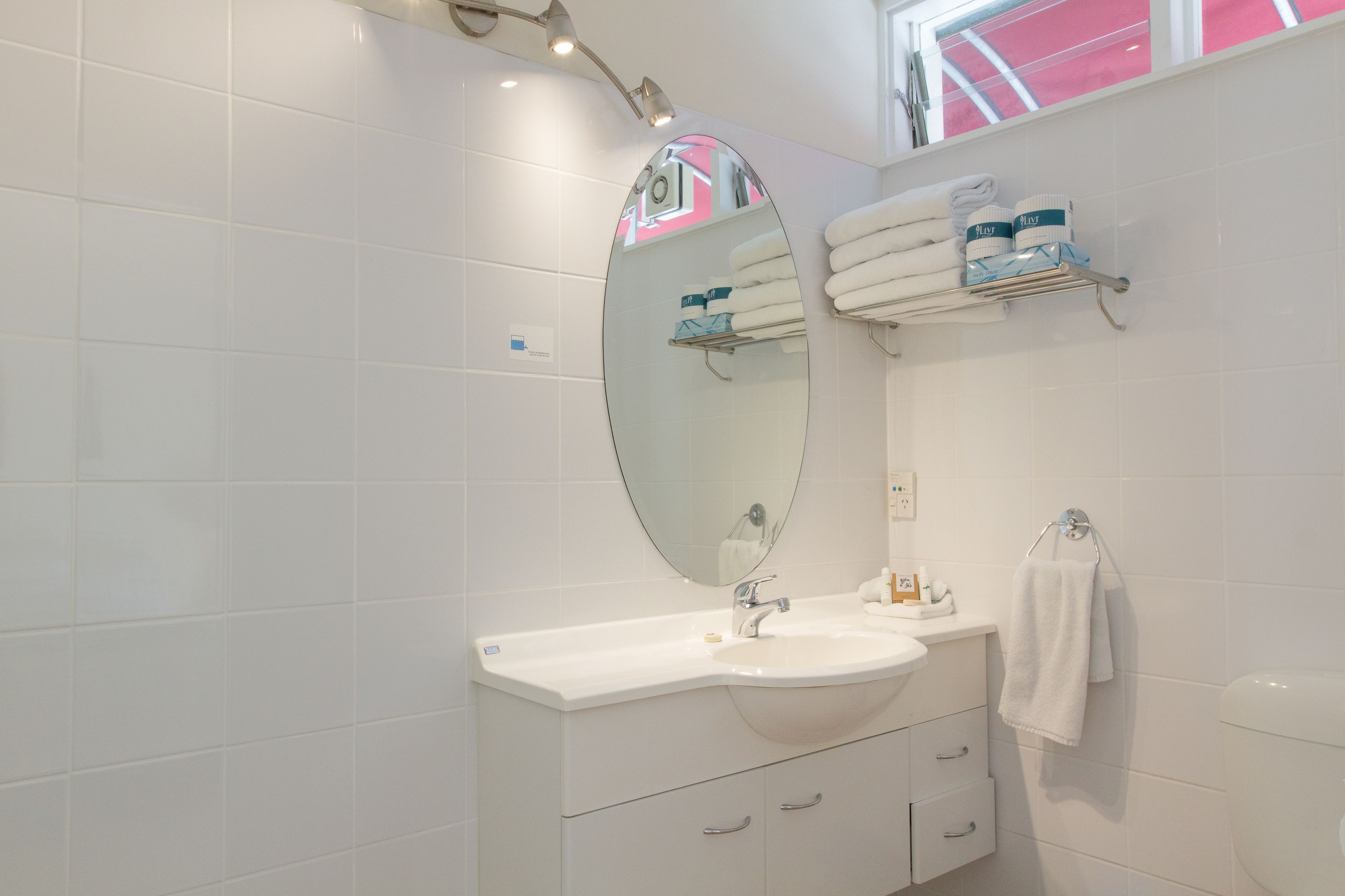 A modern bathroom with a large oval mirror, white tiles, a vanity with a sink, and a towel rack.