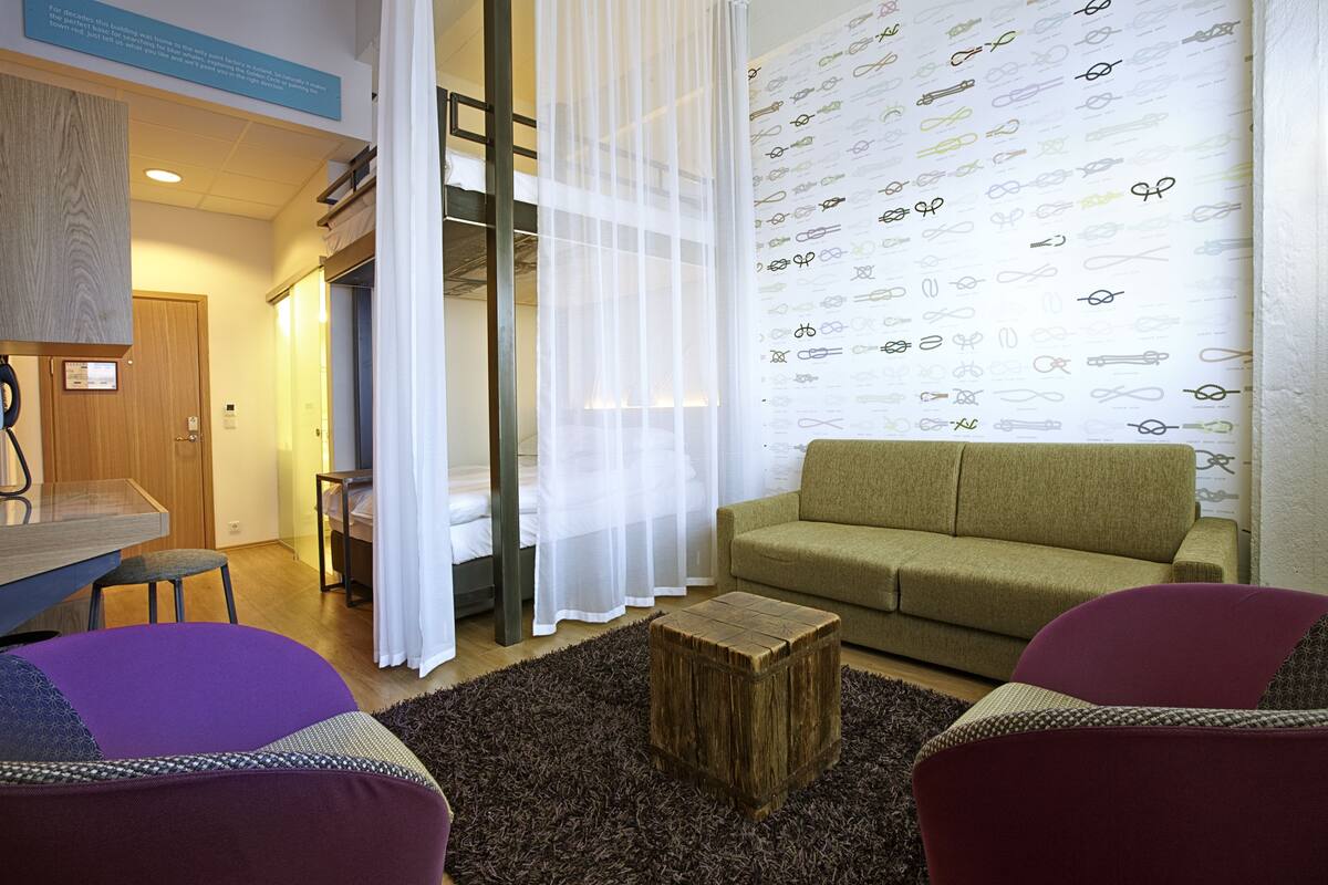 Een moderne woonkamer met een bank, een klein houten krukje en een behang met een patroon.