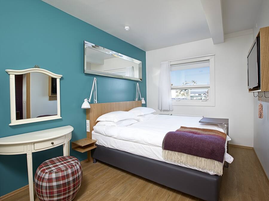 Une chambre à coucher avec un lit, une table de chevet, une chaise, un miroir et une fenêtre.