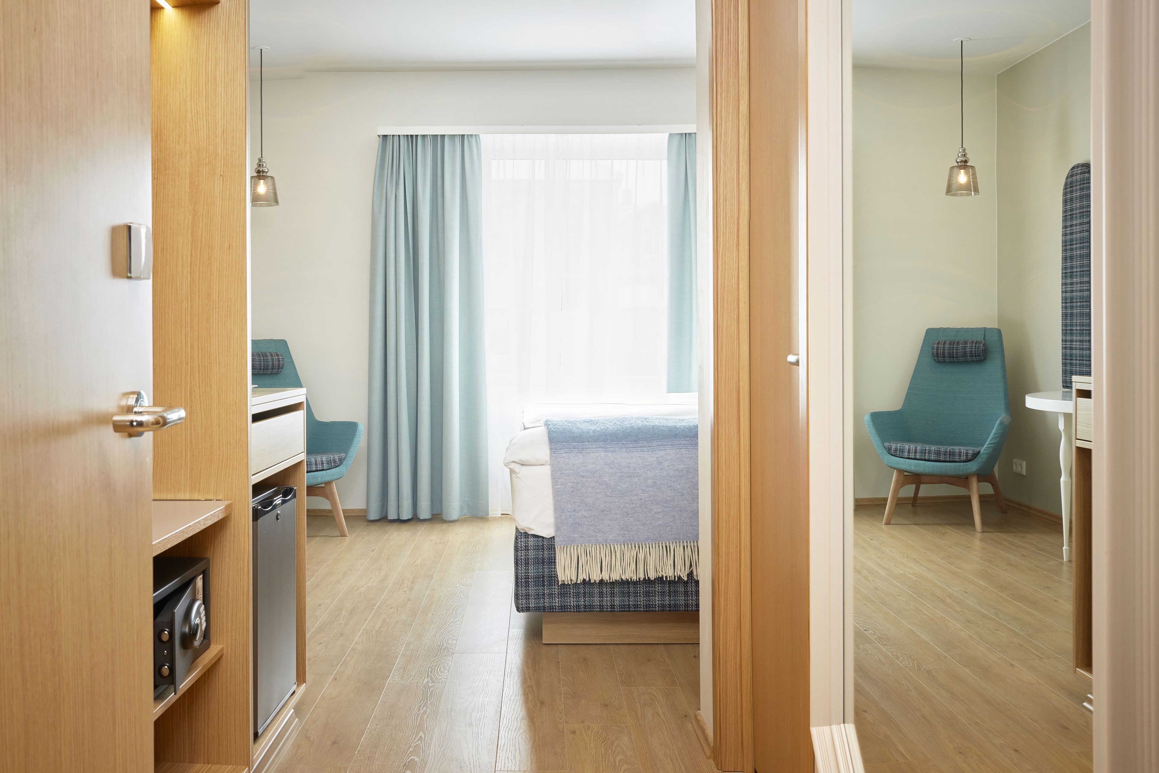 A hotel room with a bed, a desk, a chair, a small table, and a window with curtains.