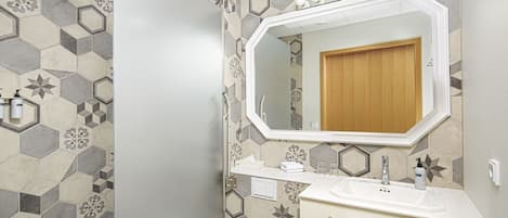 Une salle de bain avec un carrelage à motifs hexagonaux, un lavabo blanc, une porte en bois et un miroir au-dessus du lavabo.
