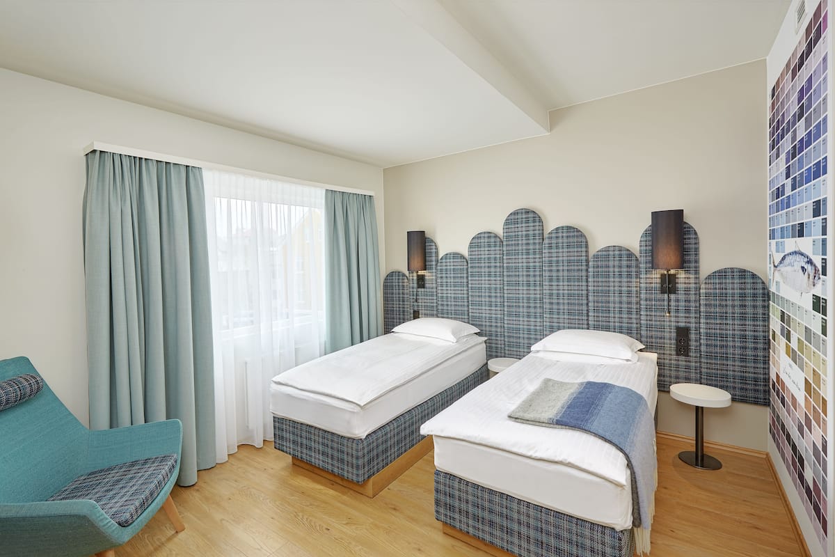 Hotelkamer met twee bedden, een klein rond tafeltje, een stoel en een muur met een kleurenpalet.