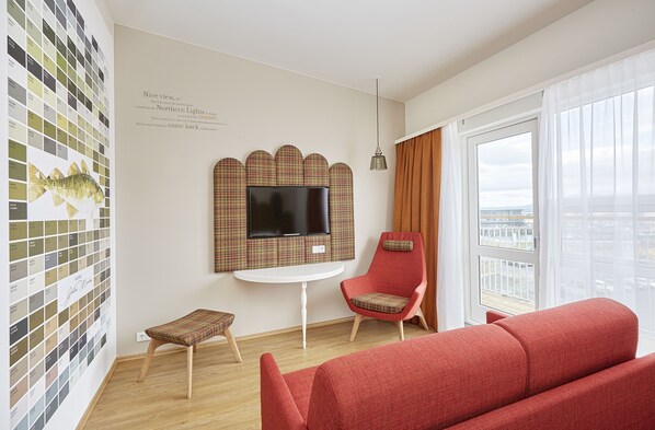Una sala de estar moderna con un sofá rojo, un sillón escocés, una mesita y un televisor instalado en una pared con estampado de cuadros.
