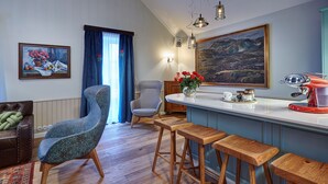 A modern kitchen with a bar area, wooden stools, a high chair, and a painting on the wall.