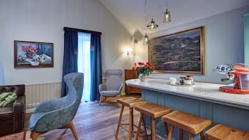 A modern kitchen with a bar area, wooden stools, a high chair, and a painting on the wall.