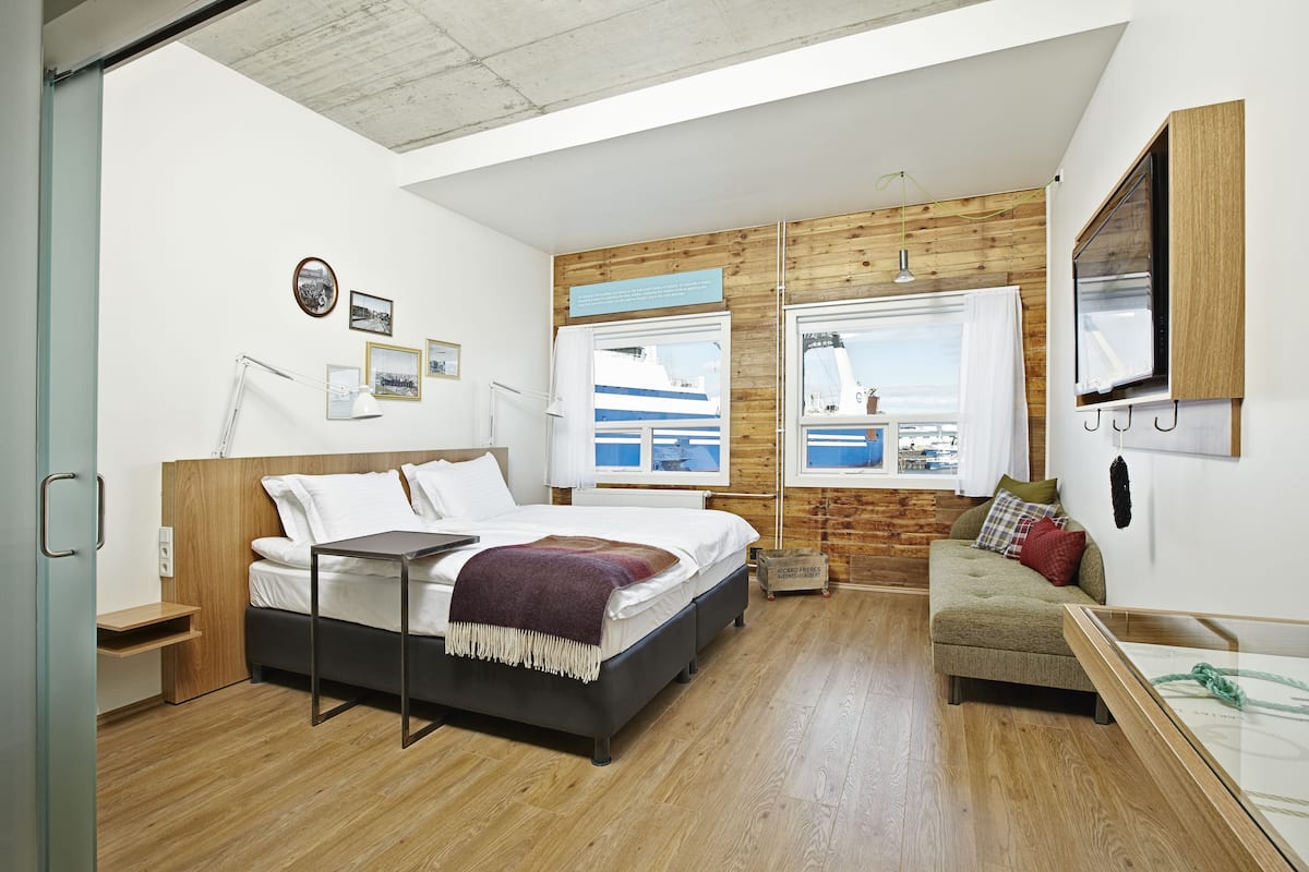 Een moderne slaapkamer met een groot bed, een bank en uitzicht op een schip door de ramen.