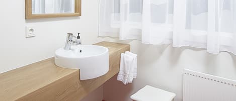 Un baño con lavamanos blanco, espejo y una toalla blanca sobre un taburete.