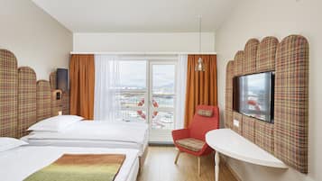 A hotel room with two beds, a television, a red chair, and a view of the city through the window.