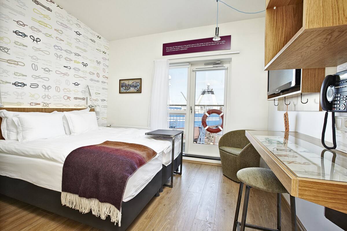 Een hotelkamer met een bed, een bureau en uitzicht op zee.
