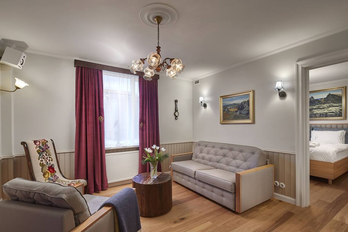 Een goed verlichte woonkamer met een bank, fauteuil en een ronde houten salontafel.