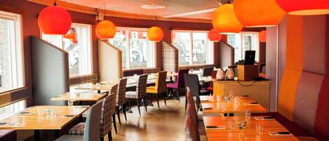 A restaurant with wooden tables and chairs, large windows, and orange hanging lights.