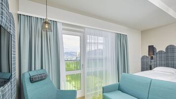 A hotel room with a large window, a bed, two sofas, and a view of a mountainous landscape.