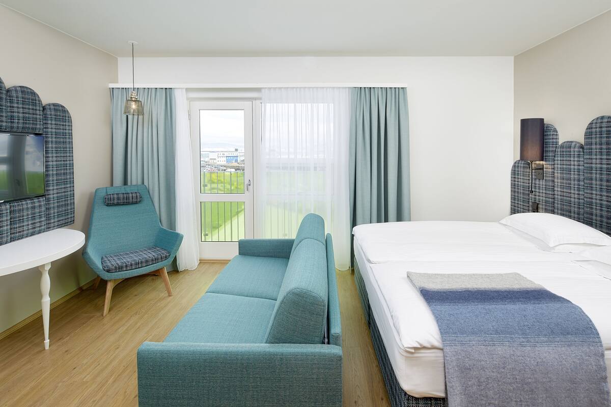Hotelkamer met een bed, een bank, een stoel, een televisie en een balkon met gordijnen.