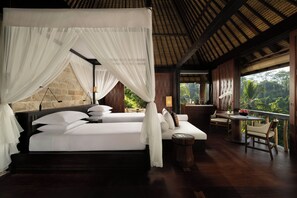 A four-poster bed with white linens and a canopy, a wooden table with chairs, and a view of the surrounding greenery. - COMO Shambhala Estate (Ubud)