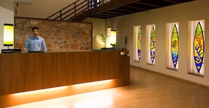 A reception desk with a wooden counter, a stone wall, and a staircase in the background. - Lemon Tree Hotel Tarudhan Valley (Taoru)
