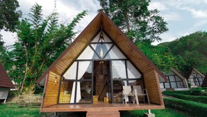 Una cabaña de madera triangular con ventanas grandes y una escalera que lleva a la entrada.