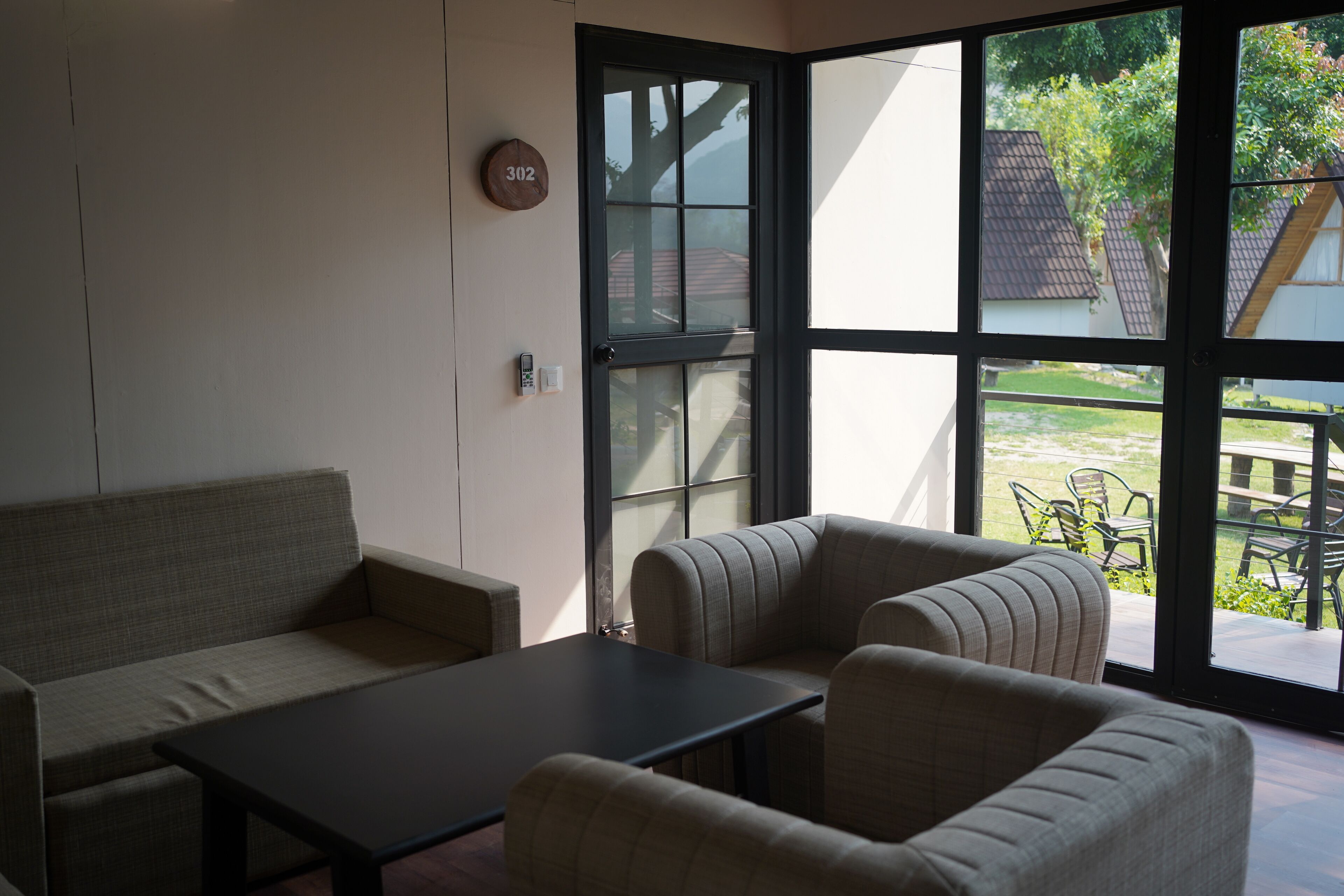 A room with a sofa, armchairs, a table, and a large window with a view of the outside.