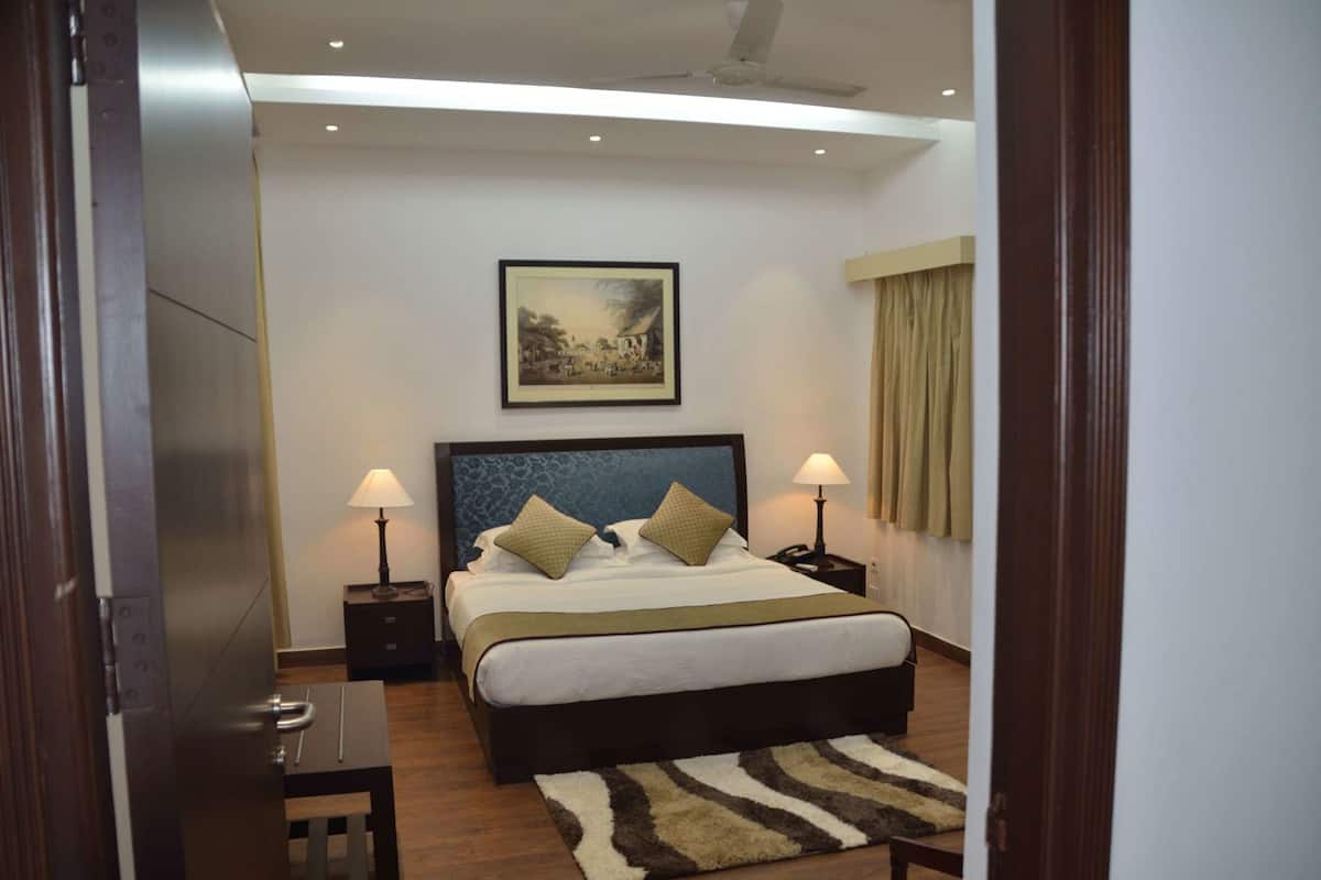 Una habitación de hotel con una cama grande, dos mesitas de noche con lámparas, un cabecero con una pintura de un paisaje y suelo de madera.