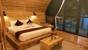 Un dormitorio de estilo cabaña con cama, almohadas, una mesita de noche y una ventana con cortinas.