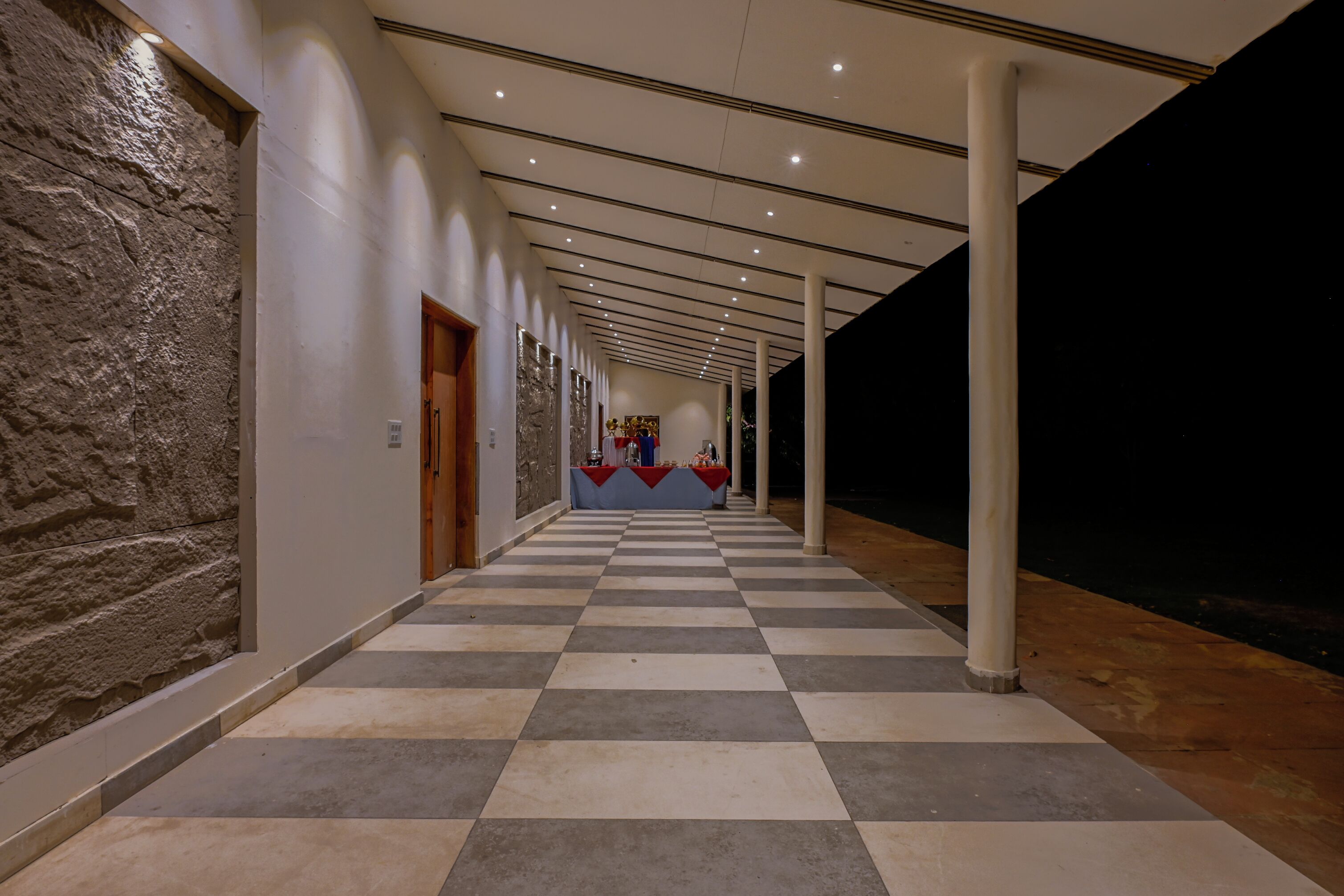 A corridor with checkered flooring, columns, and a stone wall on one side.