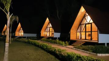 A row of triangular-roofed cabins with illuminated windows, a pathway, and a well-maintained lawn.