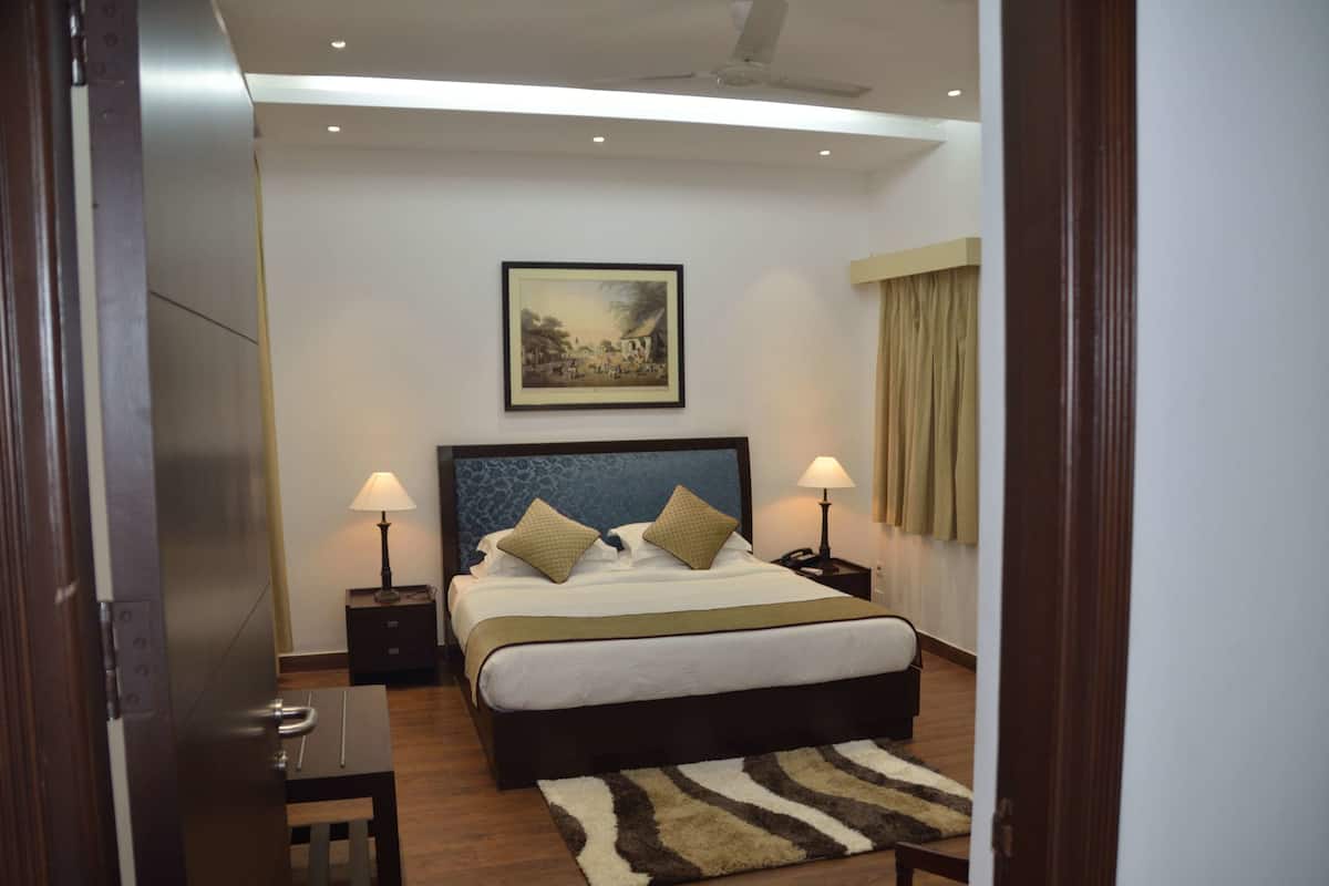 Un dormitorio con una cama grande, dos mesitas de noche con lámparas, un cuadro en la pared y una ventana con cortinas.