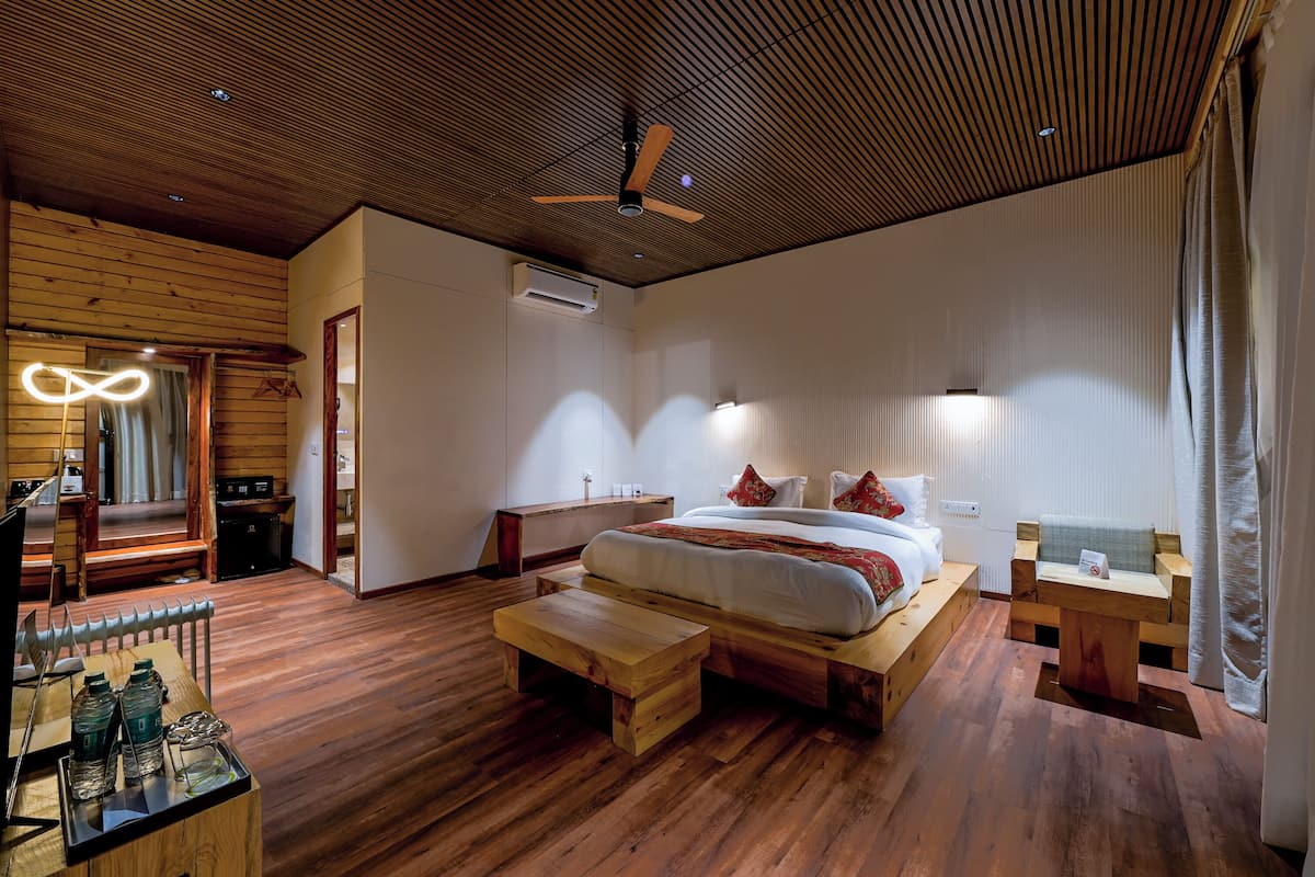 Un dormitorio moderno con techo de madera, una cama grande con almohadas, una mesita de noche, un banco de madera y un escritorio con botellas de agua.