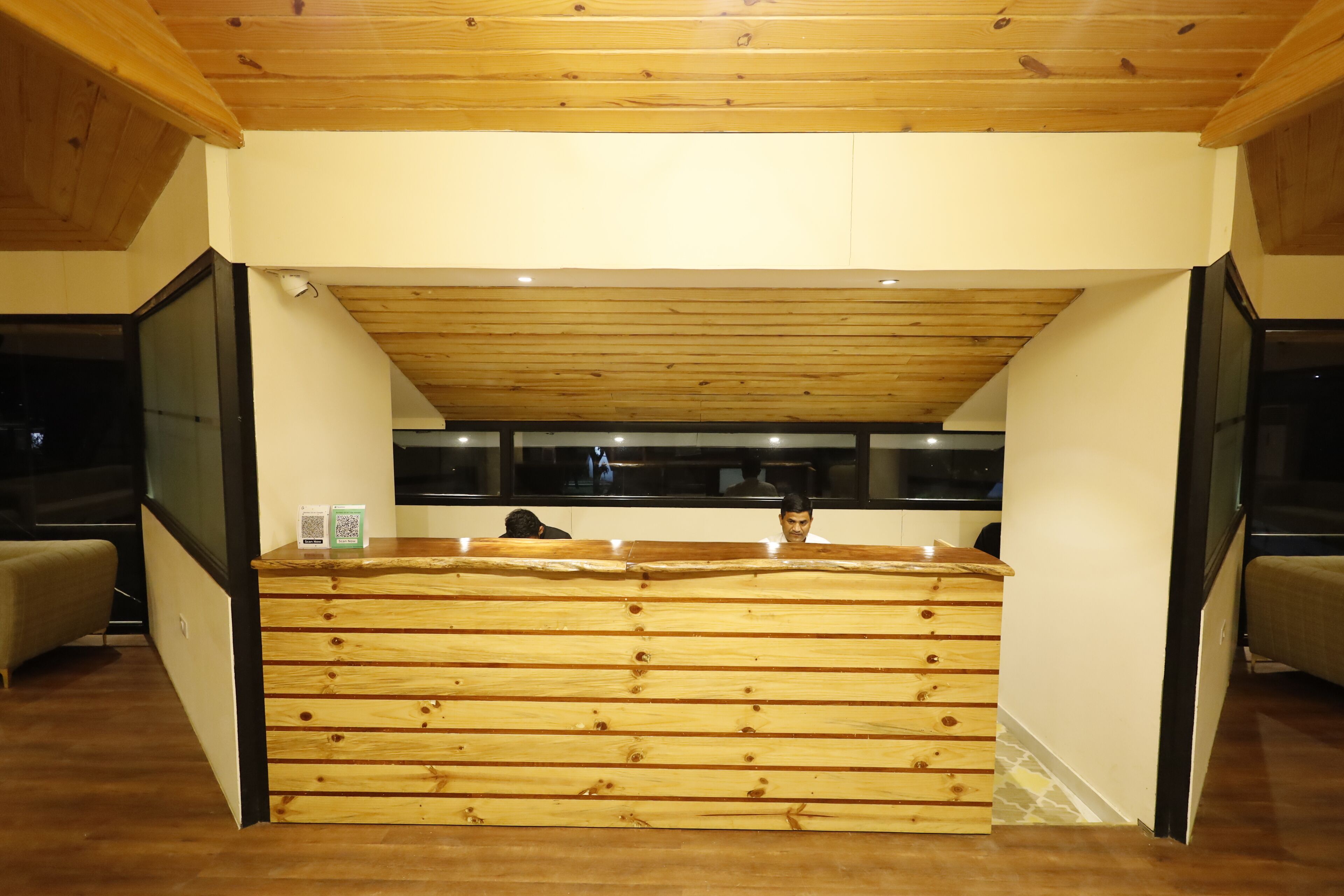 Een receptiebalie met een houten afwerking, een schuine plafond en een glazen scheidingswand.
