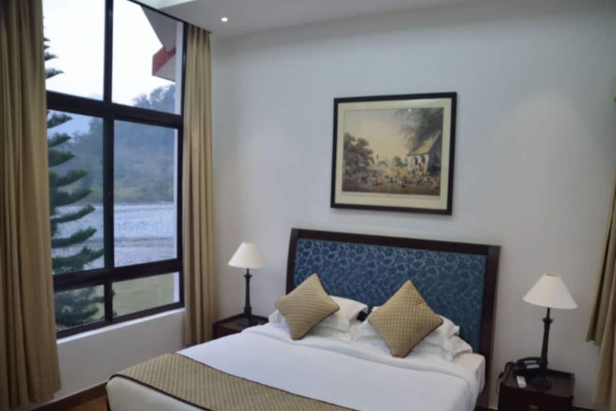 Habitación de hotel con una cama grande, dos lámparas de noche, un cuadro en la pared y una ventana con cortinas.