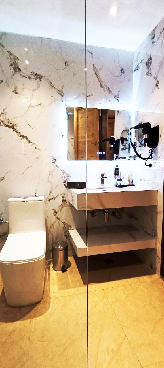 Un baño moderno con salpicadero de mármol, inodoro blanco, lavabo con espejo y un pequeño cubo de basura.