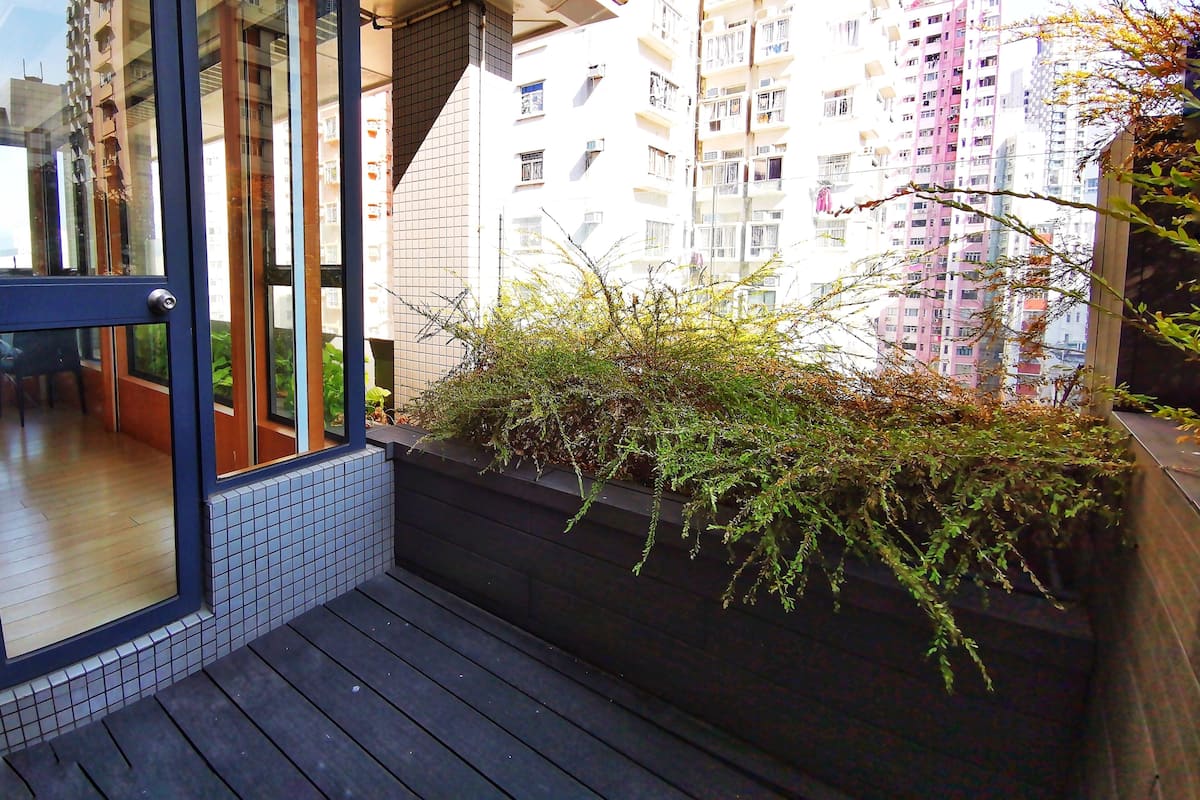 A modern apartment with a balcony, a view of neighboring high-rise buildings, and a small garden area.