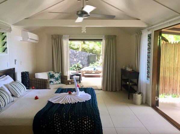 A hotel room with a bed, a ceiling fan, a window with curtains, a small table, and a view of the outdoors. - Seabreeze Resort Samoa - Exclusively for adults (Aufaga)