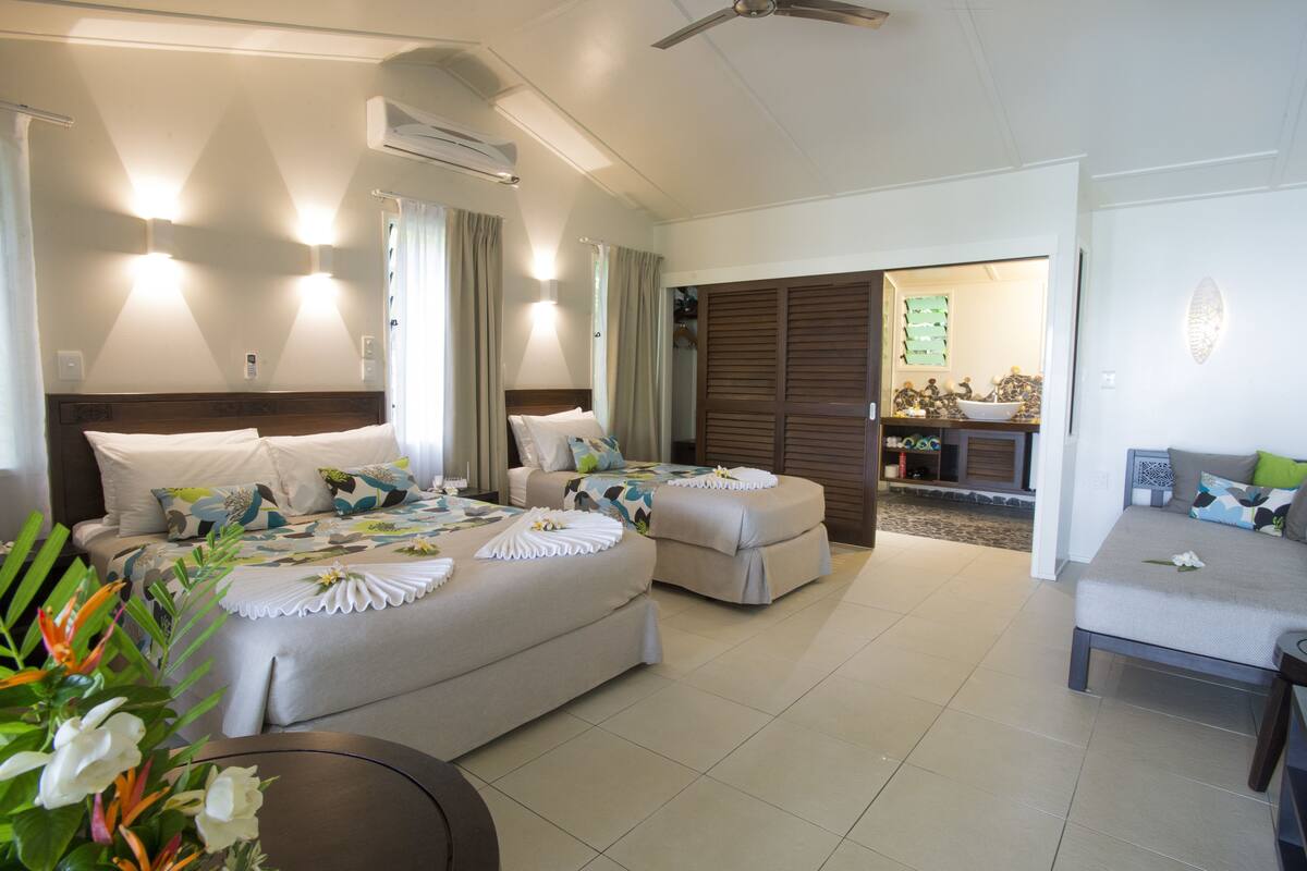 A hotel room with two beds, a sofa, a dining area, and a bathroom.