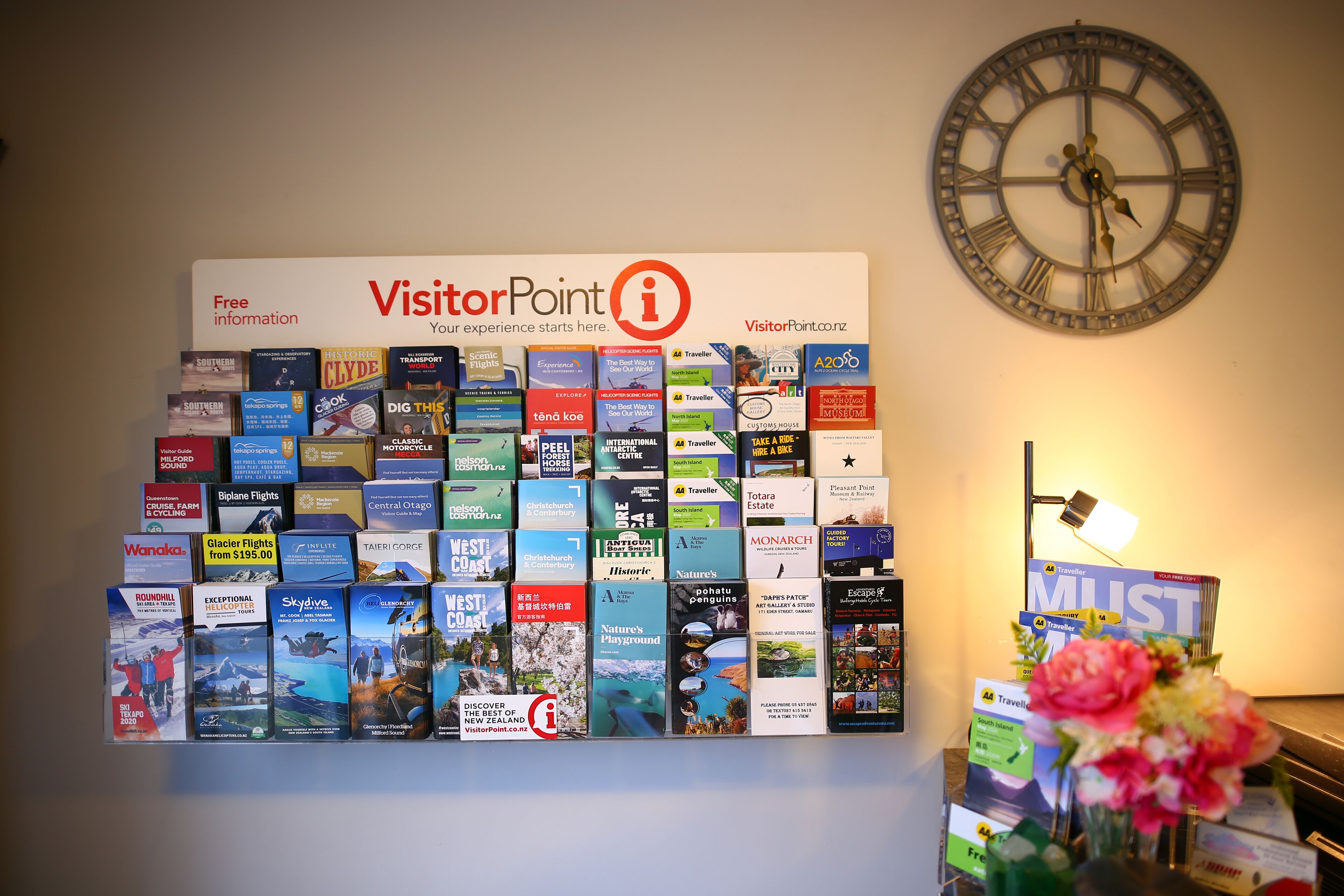A wall with a large clock and a display of travel brochures.