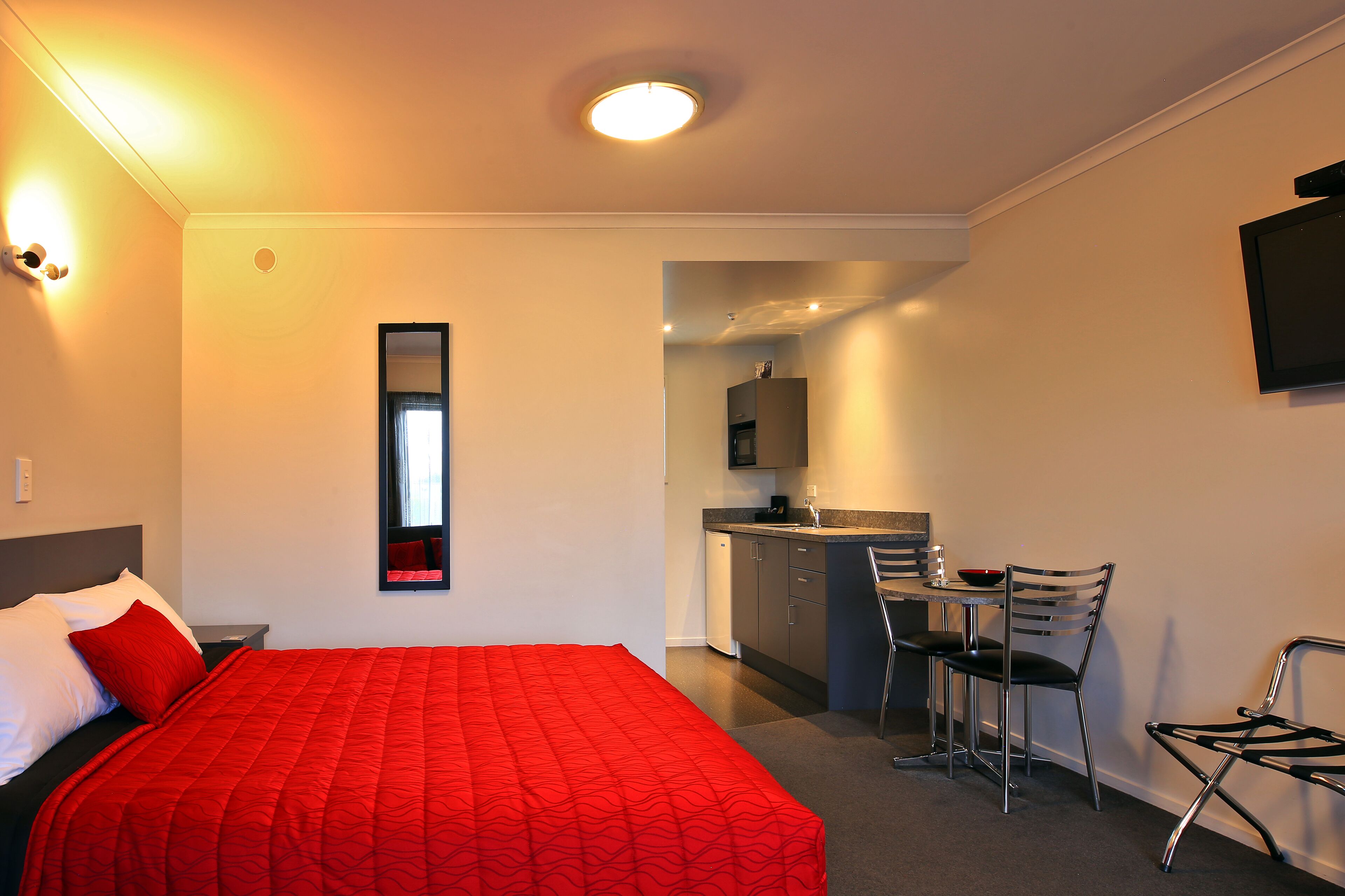 A hotel room with a bed, a desk, a chair, and a kitchenette.