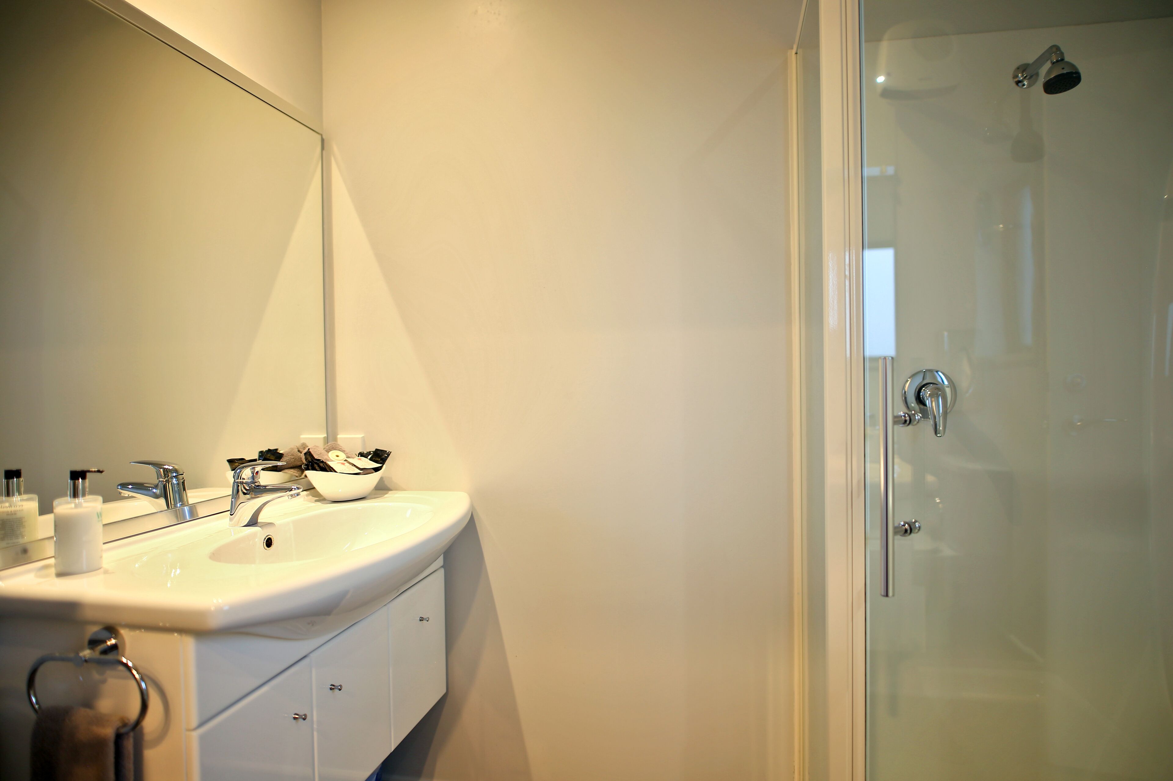 A modern bathroom with a large mirror, a sink, and a glass-enclosed shower.