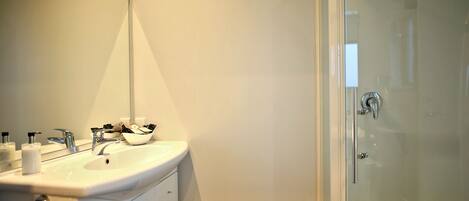 A modern bathroom with a large mirror, a sink, and a glass-enclosed shower.