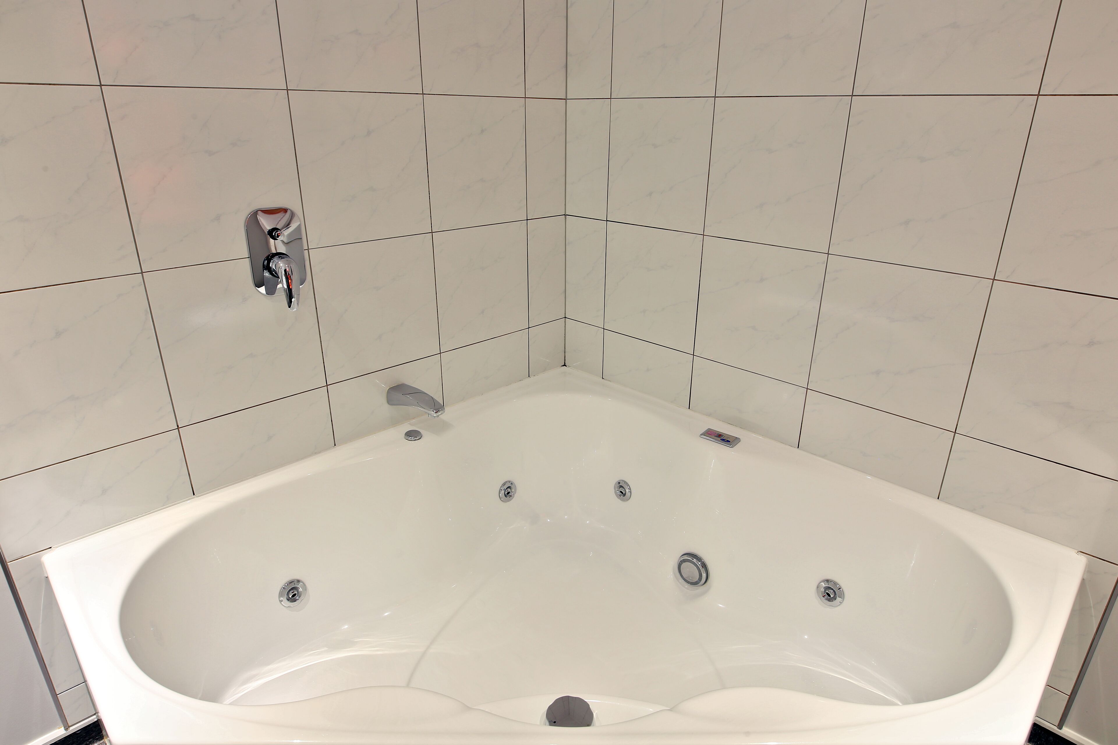 A large, rectangular bathtub with a single faucet and a drain, surrounded by white tiled walls.
