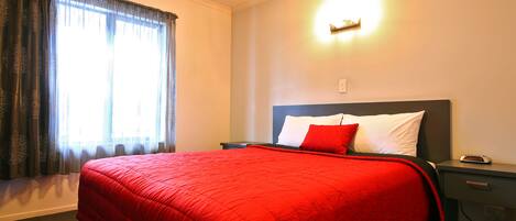 A hotel room with a large bed, a bedside table, a nightstand, and a wall-mounted light.