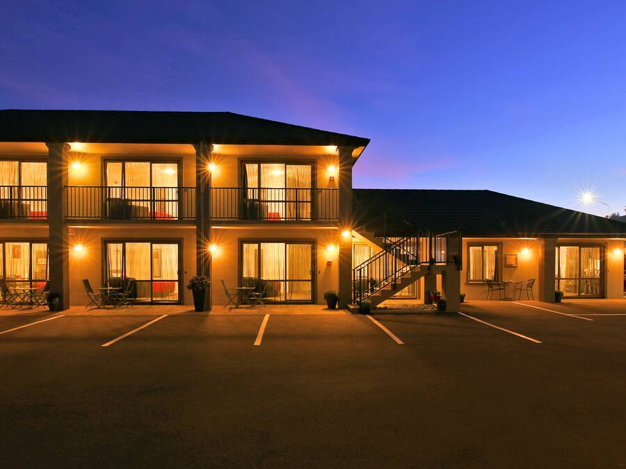 A multi-story hotel with a parking lot, outdoor seating, and a staircase leading to the entrance.